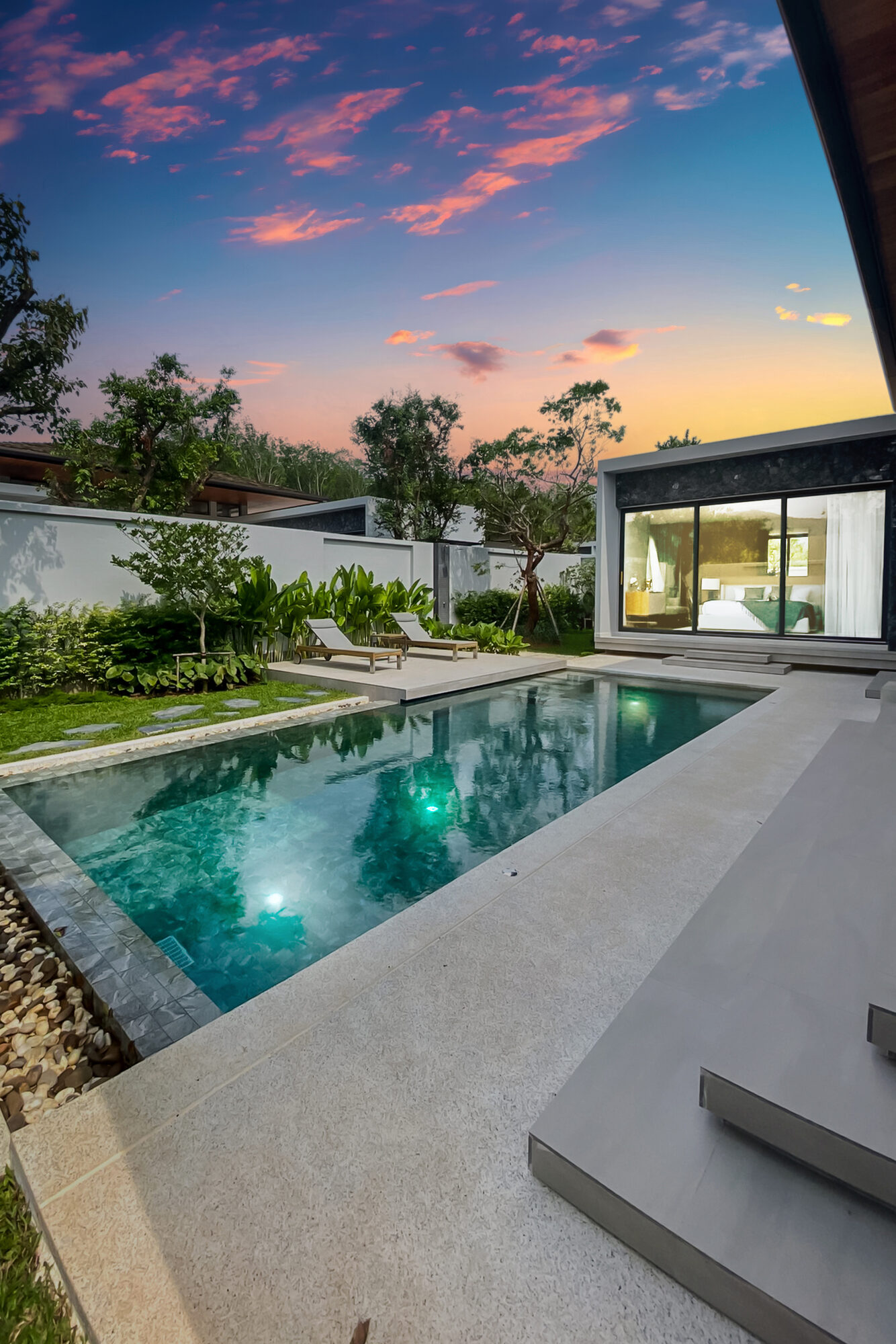 Villa Luma Botanica swimming pool at sunset with sun loungers on the lawn and tropical planting, Bang Tao Phuket