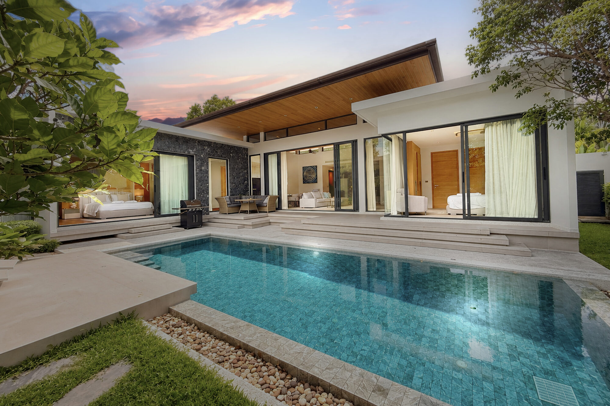 Villa Luma Botanica private pool and terrace at dusk, framed by a vaulted timber roof and glass walls opening to the living room and bedroom